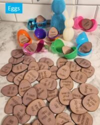 fifty dark stained wooden laser-engraved egg-shaped Easter reward tokens spread across a marble surface beside colorful open plastic Easter eggs, with rewards including build a blanket fort, bake cookies, watch your show, s'mores night, dance party, and Mom and me day