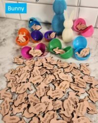 sixty-three wooden laser-engraved bunny-shaped Easter egg reward tokens spread across a marble surface beside colorful open plastic Easter eggs, with rewards including build a blanket fort, family movie night, snuggle time, zoo trip, and go to library